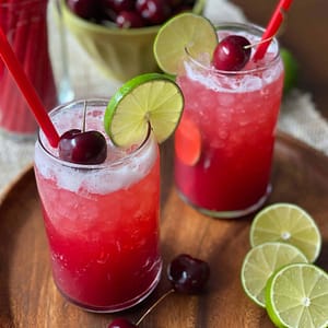 A sparkling glass of cherry limeade with ice cubes, fresh cherries, and lime slices, highlighting the sweet and fizzy citrus flavor.