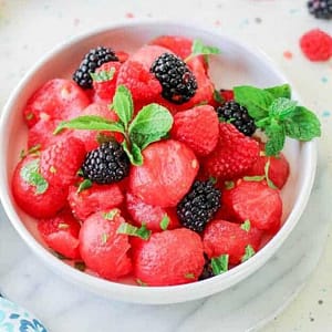 Fresh watermelon slices paired with ripe red raspberries, highlighting the sweet and tangy fruit blend.